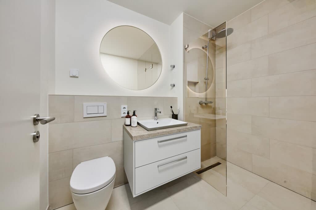 Modernes Badezimmer mit begehbarer Dusche, runden Spiegeln, hellen Fliesen und hochwertigem Waschtisch.